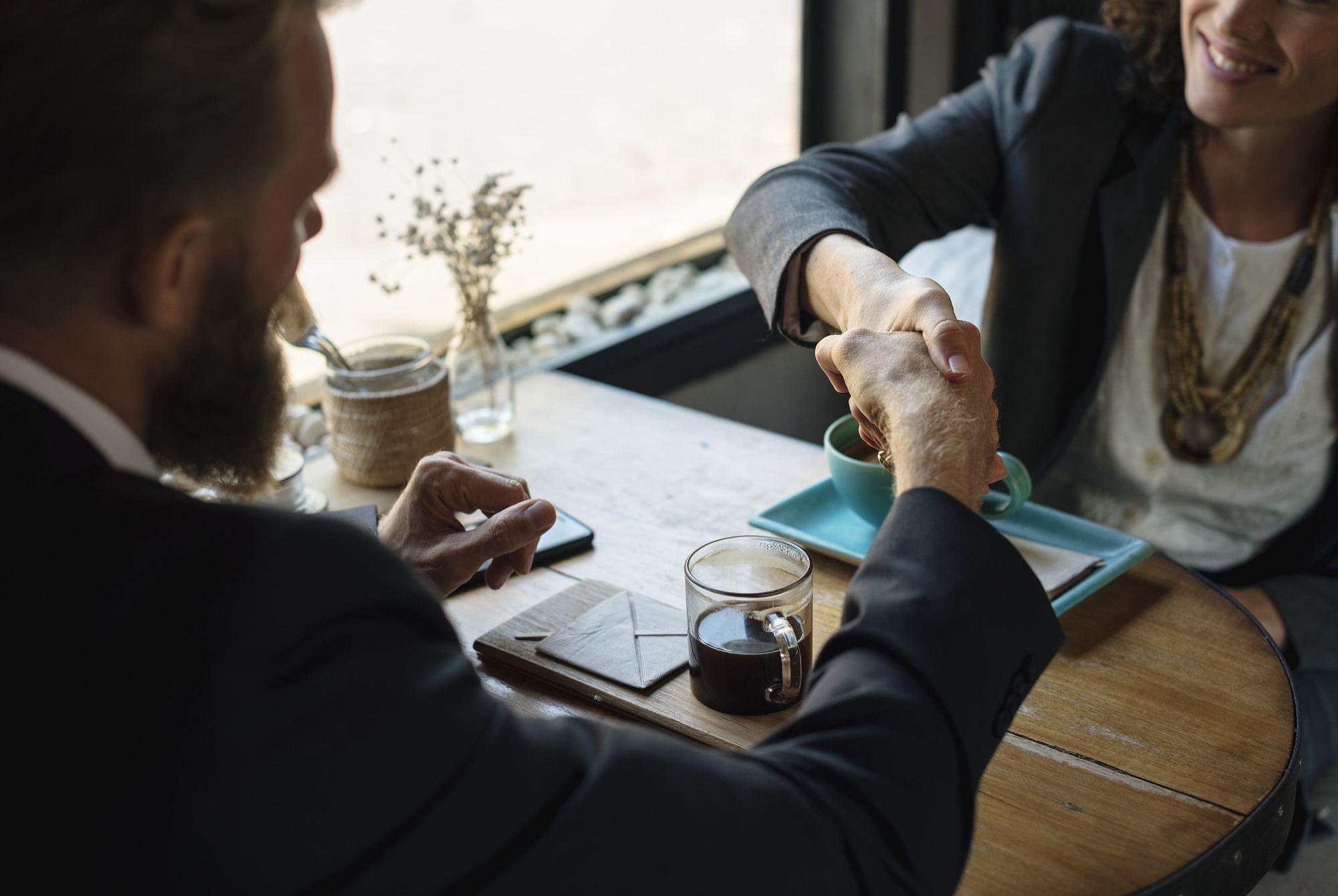 Two people shaking hands over a café table